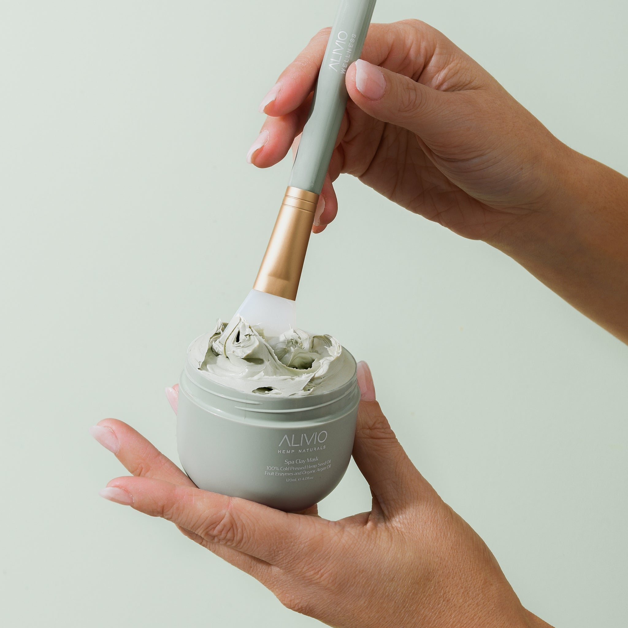 Hands showing open tub of bentonite clay mask with brush